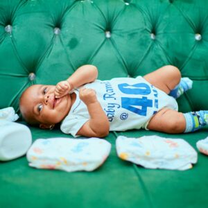 Adorable baby lying on a green sofa with diapers, showcasing a cute smile and playful demeanor.