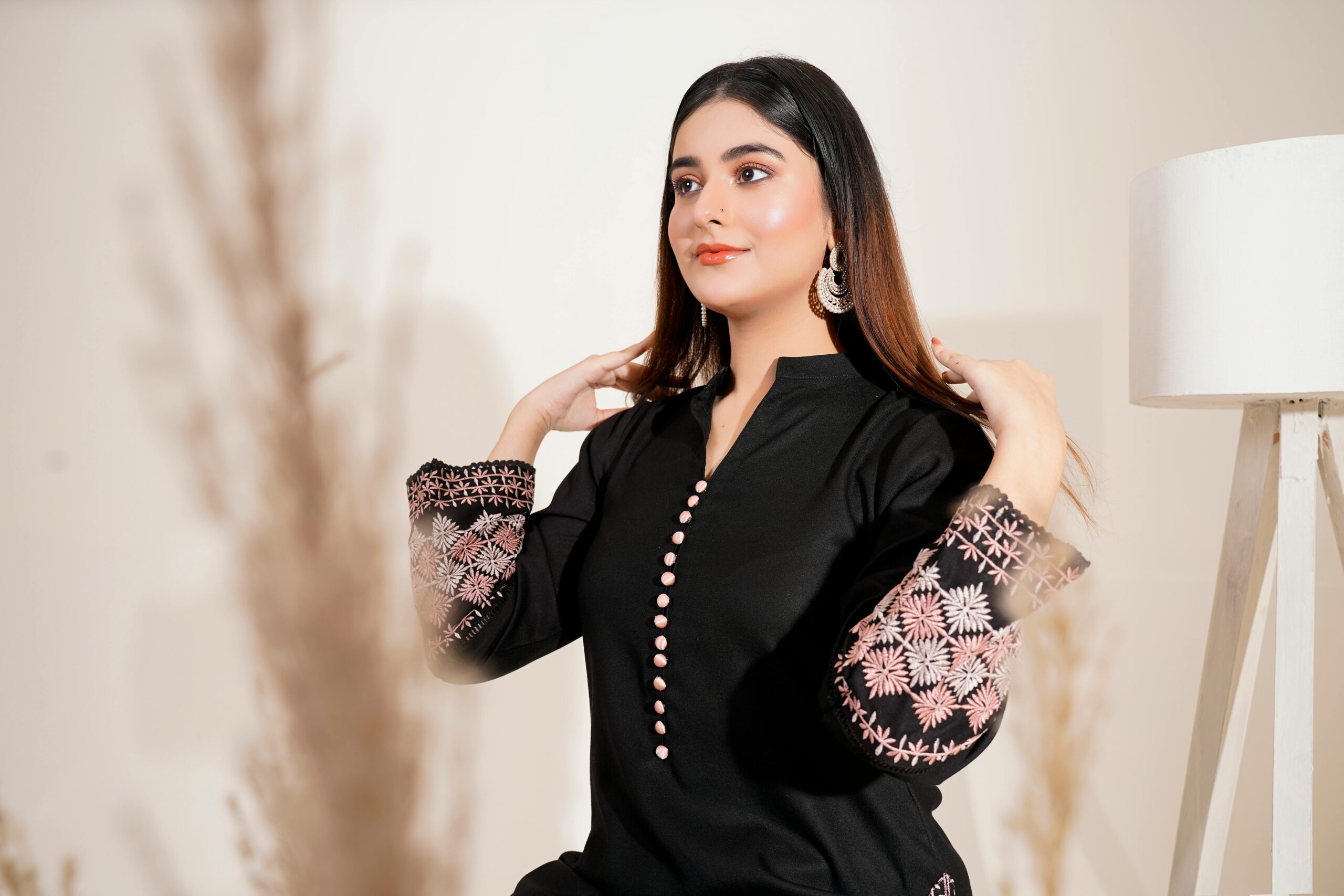 Fashionable woman in an embroidered dress posing elegantly indoors.